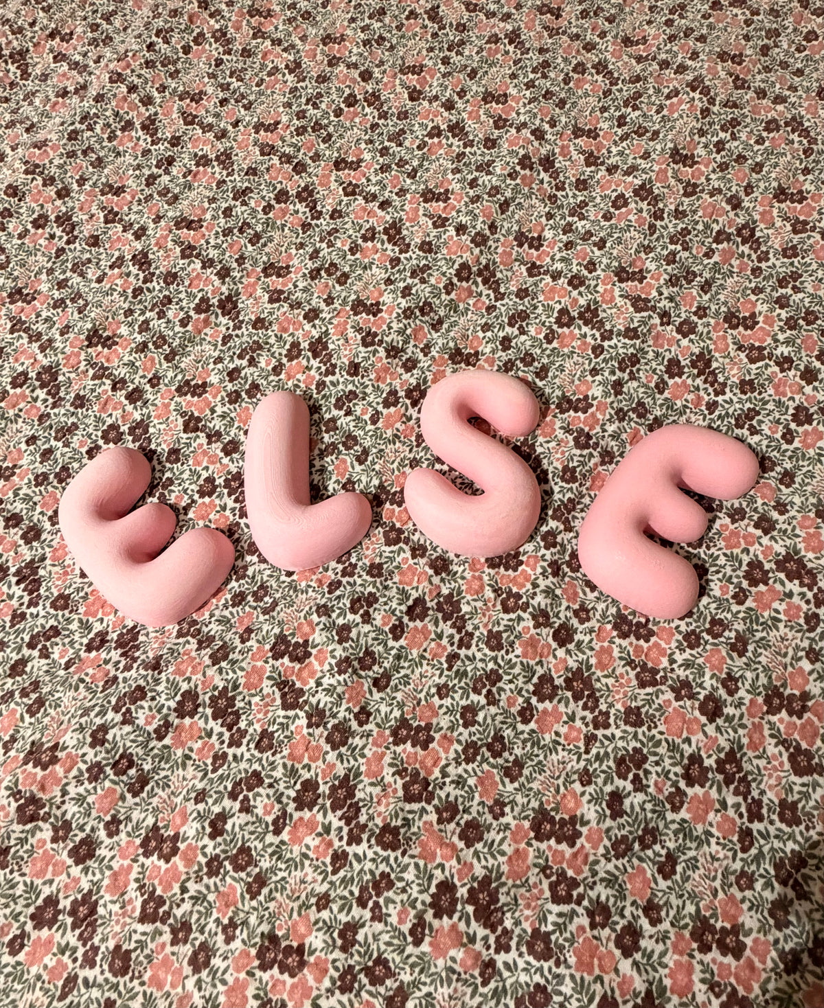 Rosa Bubble Letters som staver ELSE på blomstrete stoff